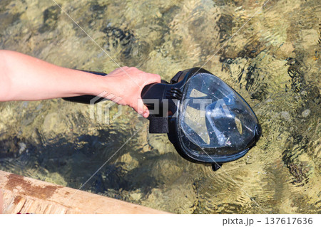 Woman cleaning her snorkeling mask in the clear blue sea, preparing for an exciting underwater adventure and enjoying the beauty of marine life 137617636