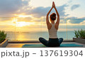 Woman practicing yoga on a mat at sunset, ocean view with clouds and greenery in the background, serene outdoor setting 137619304