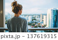 Woman with blonde hair gazes at city skyline from a balcony, modern buildings and urban landscape visible in the background 137619315
