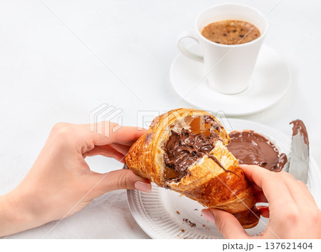 Woman breaking chocolate croissant with coffee breakfast scene 137621404