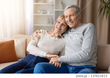 Senior couple sitting closely together on sofa at home looking away thoughtfully Senior couple sitting closely together on sofa at home looking away thoughtfully 137621613