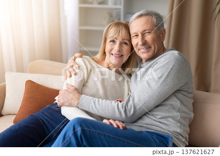 Senior couple relaxing together on sofa at home smiling warmly and embracing 137621627