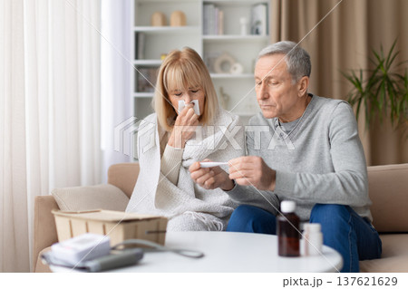 Senior couple at home checking thermometer while woman is sick and coughing Senior couple at home checking thermometer while woman is sick and coughing 137621629
