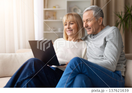 Senior couple relaxing together on sofa while using a laptop at home Senior couple relaxing together on sofa while using a laptop at home 137621639