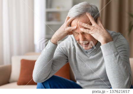 Stressed senior man sitting on couch at home holding head with hands 137621657