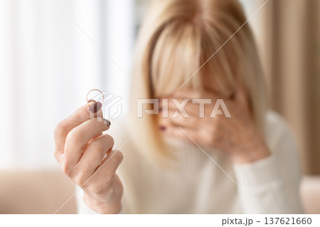 Sad senior woman holding wedding ring and covering face with hand 137621660