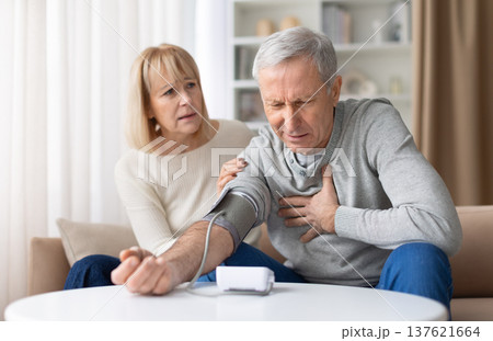 Senior man experiencing chest pain while checking blood pressure at home Senior man experiencing chest pain while checking blood pressure at home 137621664