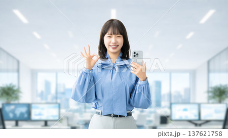 スマートフォンを持ってOKポーズをする若い女性・ビジネスウーマン 137621758