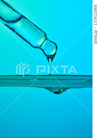 Pipette dropping blue liquid into water surface impacting 137622068