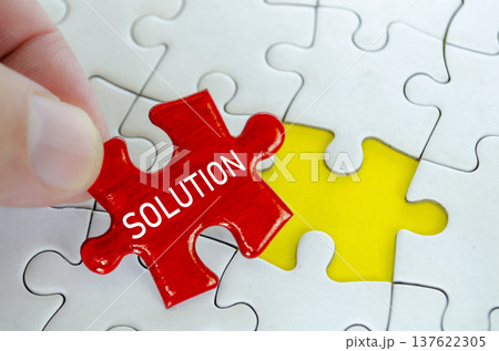 Red solution puzzle piece being placed by hand beside a yellow piece on a white jigsaw puzzle background 137622305