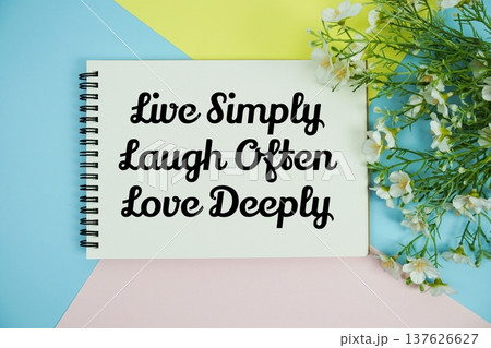 Live Simply Laugh Often Love Deeply text written on notepad with flowers decorations flat lay on multicolor pastel background Live Simply Laugh Often Love Deeply text written on notepad with flowers decorations flat lay on multicolor pastel background 137626627