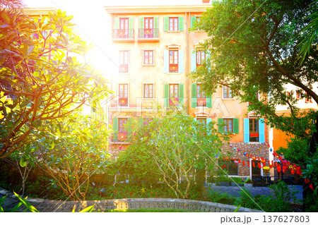 Sunlight shines on colorful buildings with plants in garden in european neighborhood. Sunlight shines on colorful buildings with plants in garden in european neighborhood. 137627803