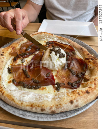 Hand cutting pizza with burrata cheese, truffle and prosciutto on crispy baked crust served on plate in restaurant setting. Restaurant marketing, gourmet food promotion, Italian cuisine menus Hand cutting pizza with burrata cheese, truffle and prosciutto on crispy baked crust served on plate in restaurant setting. Restaurant marketing, gourmet food promotion, Italian cuisine menus 137627845