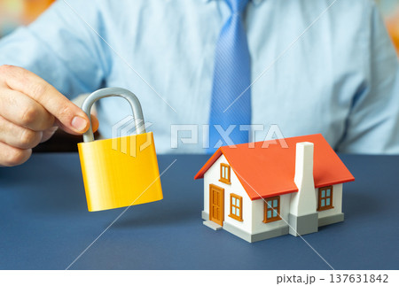 A house and a padlock in a man's hand. Ensuring property safety and home protection. Security systems, insurance coverage and cooperation with law enforcement to prevent burglary A house and a padlock in a man's hand. Ensuring property safety and home protection. Security systems, insurance coverage and cooperation with law enforcement to prevent burglary 137631842