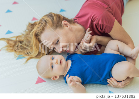 Mother and baby lying on a soft play mat at home, playing, talking and sharing a joyful moment together. Authentic family lifestyle, early childhood development and emotional bonding. Parenting and Mother and baby lying on a soft play mat at home, playing, talking and sharing a joyful moment together. Authentic family lifestyle, early childhood development and emotional bonding. Parenting and 137631882