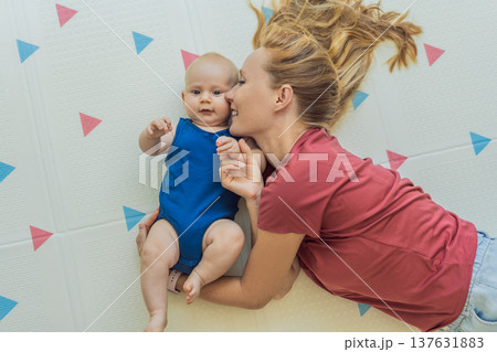Mother and baby lying on a soft play mat at home, playing, talking and sharing a joyful moment together. Authentic family lifestyle, early childhood development and emotional bonding. Parenting and Mother and baby lying on a soft play mat at home, playing, talking and sharing a joyful moment together. Authentic family lifestyle, early childhood development and emotional bonding. Parenting and 137631883