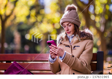 Woman with anorexia using phone in park during autumn 137631965