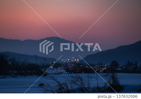 静寂に包まれた雪の里山から望む夕焼け空と遠くの街の灯り 静寂に包まれた雪の里山から望む夕焼け空と遠くの街の灯り 137632006