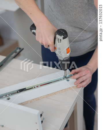 A Caucasian woman uses a screwdriver to tighten a screw while assembling a cabinet. A Caucasian woman uses a screwdriver to tighten a screw while assembling a cabinet. 137632015