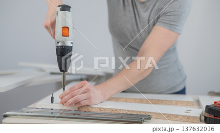 A Caucasian woman uses a screwdriver to tighten a screw while assembling a cabinet. 137632016