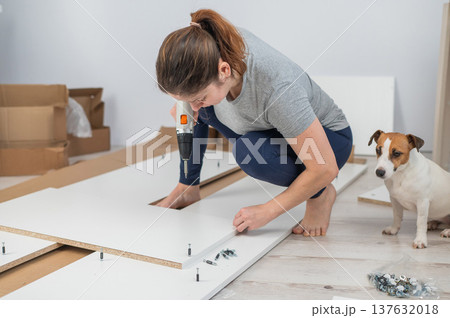 A Caucasian woman uses a screwdriver to tighten a screw while assembling a cabinet. 137632018
