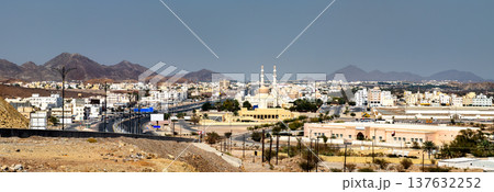 A panoramic cityscape of Rustaq, Oman, showcasing the Sultan Qaboos Mosque and the rugged Hajar Mountains under a clear blue sky. A panoramic cityscape of Rustaq, Oman, showcasing the Sultan Qaboos Mosque and the rugged Hajar Mountains under a clear blue sky. 137632252