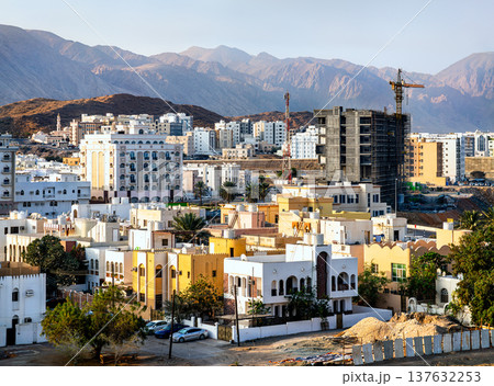 Panoramic view of the Al Khuwair district in Muscat, Oman, showing a mix of residential buildings and new construction projects against the backdrop of the rugged Hajar Mountains. 137632253