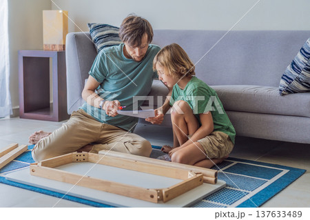 Father and his son assembling a table together in the living room at home. Meaningful family moment showing teamwork, learning and support. Fatherhood, home improvement and bonding through shared Father and his son assembling a table together in the living room at home. Meaningful family moment showing teamwork, learning and support. Fatherhood, home improvement and bonding through shared 137633489