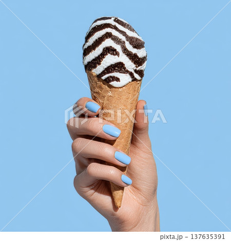 A woman's manicured hand holds an ice cream cone with white and dark stripes reminiscent of a zebra. 137635391