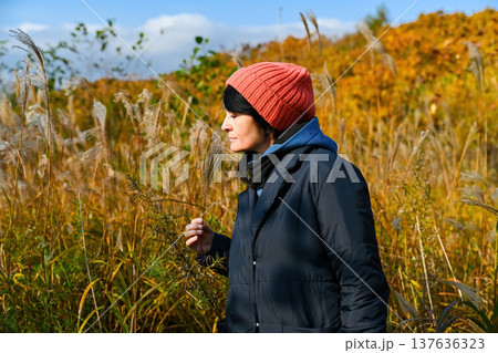 50 years old Russian woman smelling a wild grass plant in autumn field, mindful moment in nature, Far East of Russia. 50 years old Russian woman smelling a wild grass plant in autumn field, mindful moment in nature, Far East of Russia. 137636323