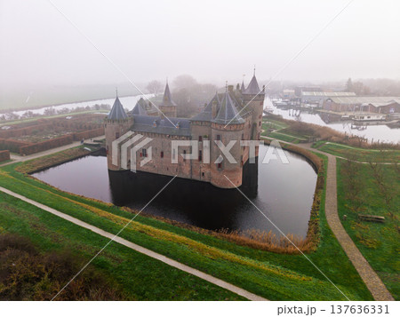 Stunning aerial view of Muiderslot Castle, a medieval fortress in the Netherlands, surrounded by a water filled moat on a foggy morning. Atmospheric European history and heritage landmark. Stunning aerial view of Muiderslot Castle, a medieval fortress in the Netherlands, surrounded by a water filled moat on a foggy morning. Atmospheric European history and heritage landmark. 137636331
