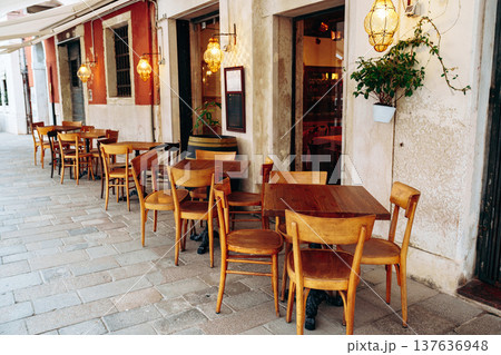Empty wooden tables and chairs outside a restaurant on a quiet street in Italy Empty wooden tables and chairs outside a restaurant on a quiet street in Italy 137636948