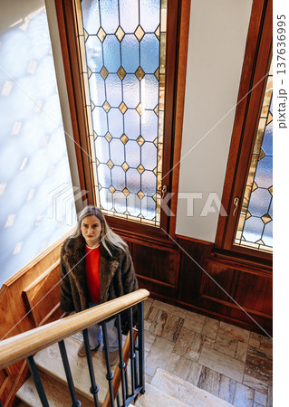 Woman climbs stairs in a building with stained glass windows during daylight hours Woman climbs stairs in a building with stained glass windows during daylight hours 137636995