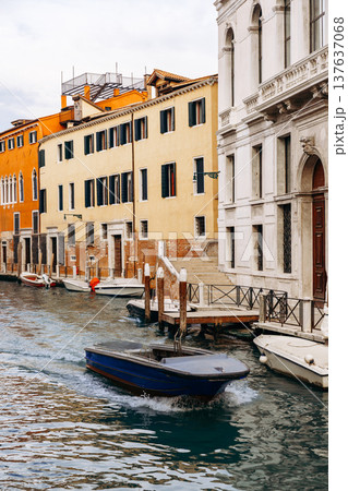 Boats move along a canal in Venice near buildings on a cloudy day 137637068