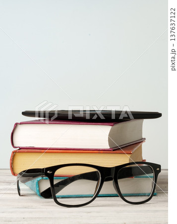 Stack of books with glasses and a notebook on a wooden table in a quiet room setting Stack of books with glasses and a notebook on a wooden table in a quiet room setting 137637122