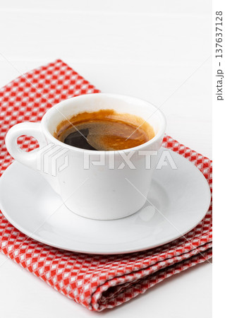 Freshly brewed espresso served on a white plate with a red checkered napkin 137637128
