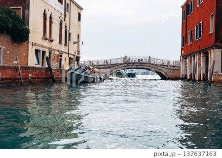 View of a boat near a bridge in a narrow canal in Venice on a cloudy day View of a boat near a bridge in a narrow canal in Venice on a cloudy day 137637163