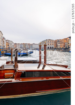 Wooden boat is docked in Venice's canal near historic buildings during a cloudy day Wooden boat is docked in Venice's canal near historic buildings during a cloudy day 137637285