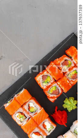 Sushi rolls arranged on a black serving board with garnishes on a gray surface Sushi rolls arranged on a black serving board with garnishes on a gray surface 137637389