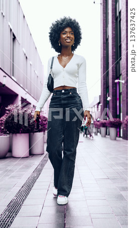 Woman walks on sidewalk in urban area with plants and buildings around in the afternoon 137637425