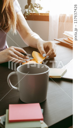 Person is working with sticky notes and a cup on a table near a window during daylight hours Person is working with sticky notes and a cup on a table near a window during daylight hours 137637426