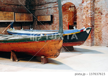 Old boats displayed in a historical building with brick walls and artifacts in the background Old boats displayed in a historical building with brick walls and artifacts in the background 137637615
