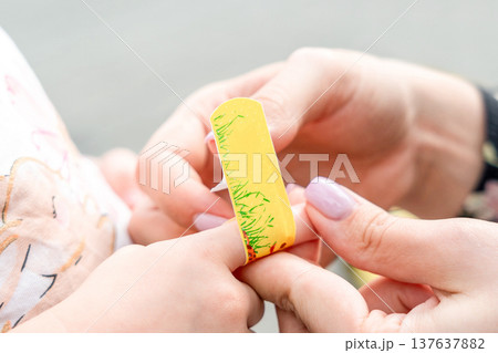 Child finger injury. Toddler receiving adhesive support outdoors. Family wellbeing concept. 137637882