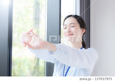 新緑の会社の窓際で伸びやストレッチする休憩するビジネスシーンの女性 スッキリして気分爽快 新緑の会社の窓際で伸びやストレッチする休憩するビジネスシーンの女性 スッキリして気分爽快 137637955