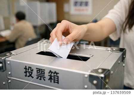 投票所で投票箱に投票用紙を入れる女性の手 137639509