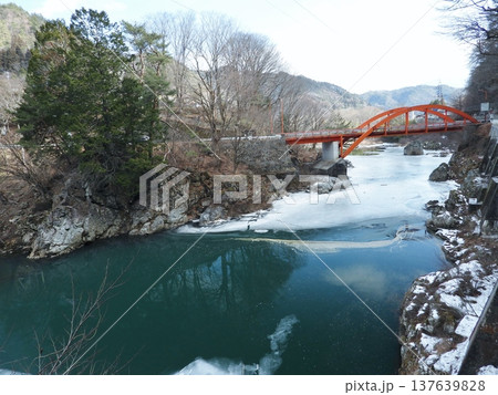 雪の王滝川に架かる赤い色の常盤橋と早春の川の景色 137639828