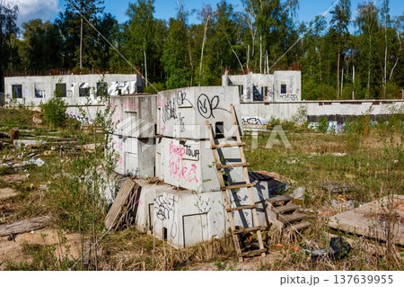 Youth find adventure at an abandoned construction site, where concrete blocks form a makeshift playground. Overgrown wilderness surrounds the unfinished buildings 137639955