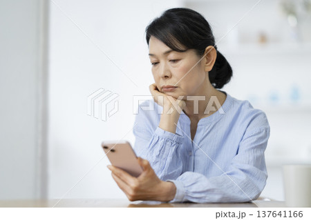 スマートフォンを見ながら考え込む50代後半の女性 スマートフォンを見ながら考え込む50代後半の女性 137641166