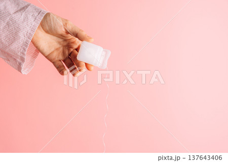 Hand holding dental floss container with floss strand on pink background, minimal dental hygiene concept 137643406