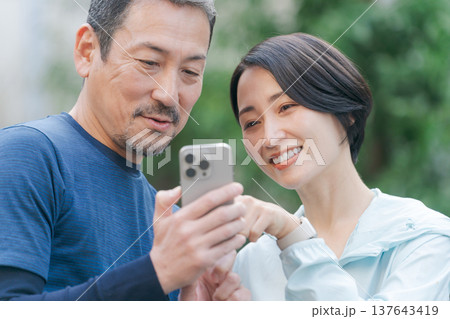 スマホを見るトレーニングウェアの夫婦 スマホを見るトレーニングウェアの夫婦 137643419